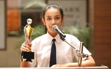 Schoolgirl raising trophy and giving speech at awards ceremony