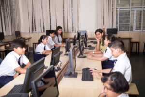 Happy teacher helping students at computer class in primary school