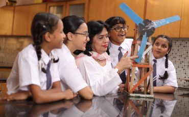 Secondary Or High School Students Studying Wind Turbines In Science Class With Teacher. Girls are excited to explore lab project. Electricity generate
